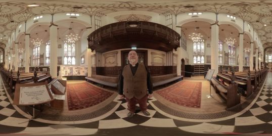 Markus Dünzkofer stands in the middle of St Johns Church, the church is ornate.
